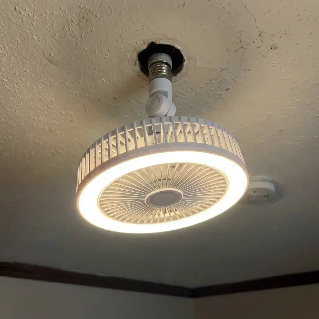 Ventilador de techo LED sujetado en las manos, aún en su caja, frente a la lámpara de un dormitorio